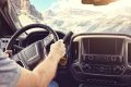 Man holding the steering wheel driving a car or truck on a rural road through the mountains